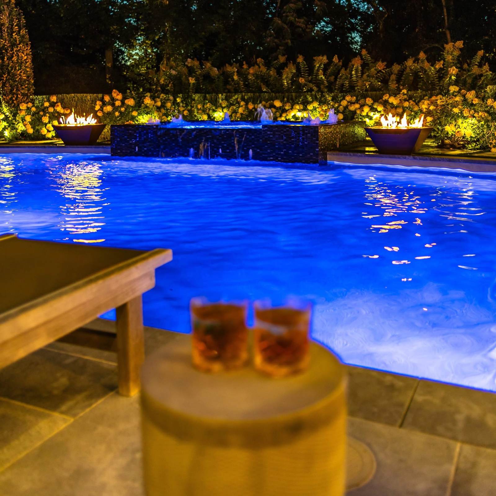 Custom pool and water feature illuminated at night with fire bowls and landscape lighting